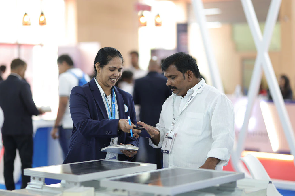 Exhibitor presenting products to several attendees at a table inside a booth during Roof India 2025