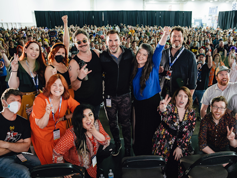 Cast of voice actors from My Hero Academia posing for a group photo with the audience in the background.