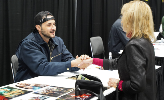 Tomer Capone holds a fan's hand with both of his as they chat. He smiles as he greets her.