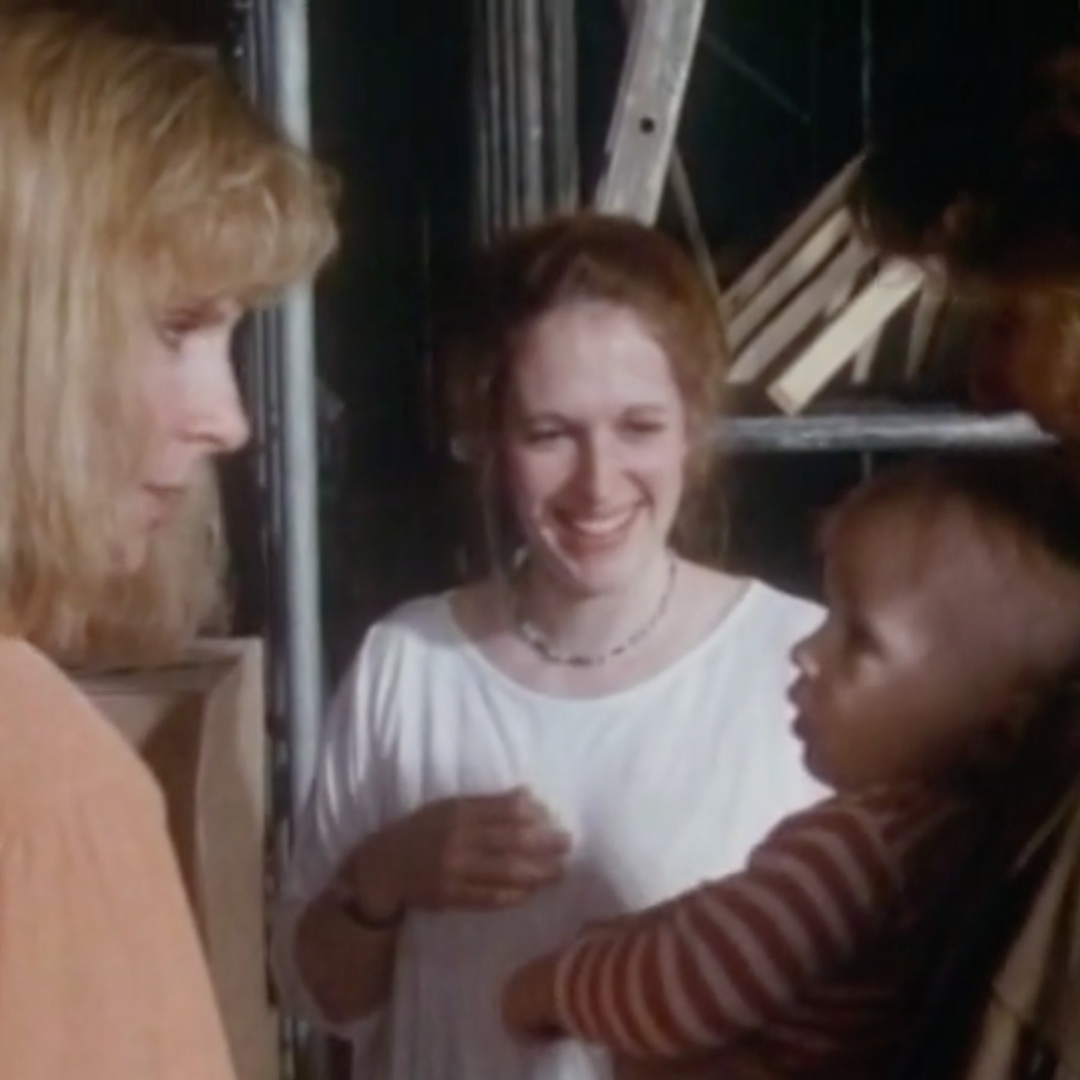 Gates McFadden looking at a baby in a stripped shirt. In between them is a smiling woman.