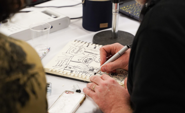 A comic artist creates a piece during a Sketch Duel, drawing Finn the Human from Adventure time in black ink.