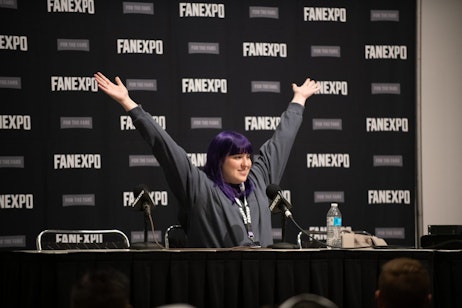 An excited Megan Shipman of SpyxFamily speaks to the crowd at her panel. Her arms outstreched in the air as she does her character voice.