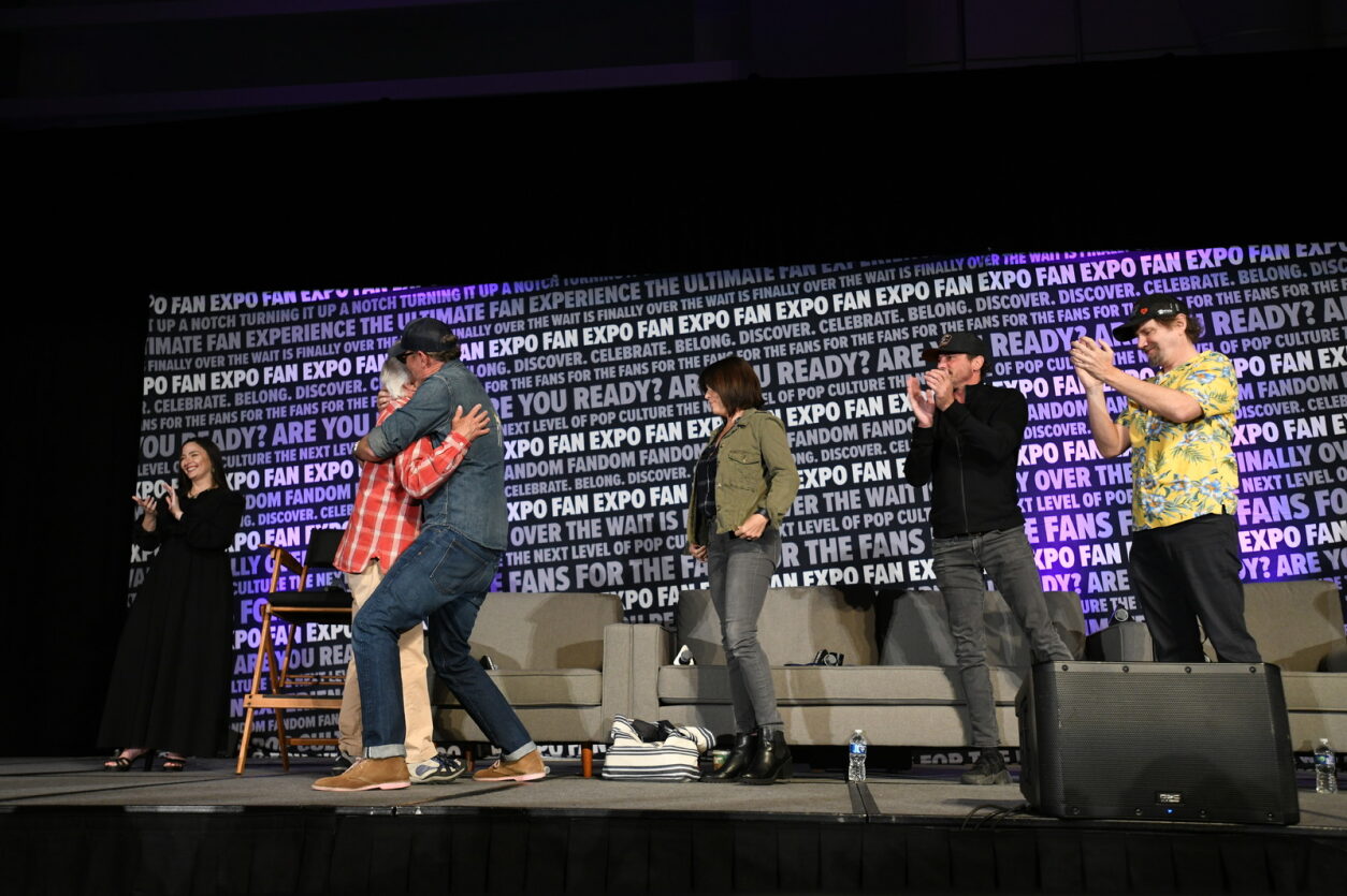 After a heartfelt greeting, Henry Winkler gives a hug to each member of the Scream cast. First is Matthew, while Neve, Jamie, and Skeet clap for Henry's contribution to their panel.