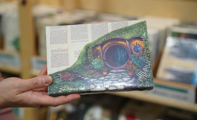 A hobbit hole is painted on passages from The Hobbit book. The vendor holds it from the left side.