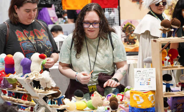 A fan shops home made crochet goods from a vendor. Plants, characters, and items from pop culture are all made of yarn.