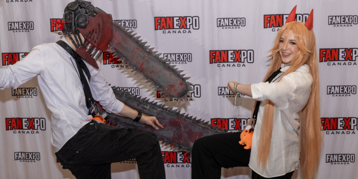 Cosplayers dressed as Denji and Power from Chainsaw Man pose together as if walking towards each other.