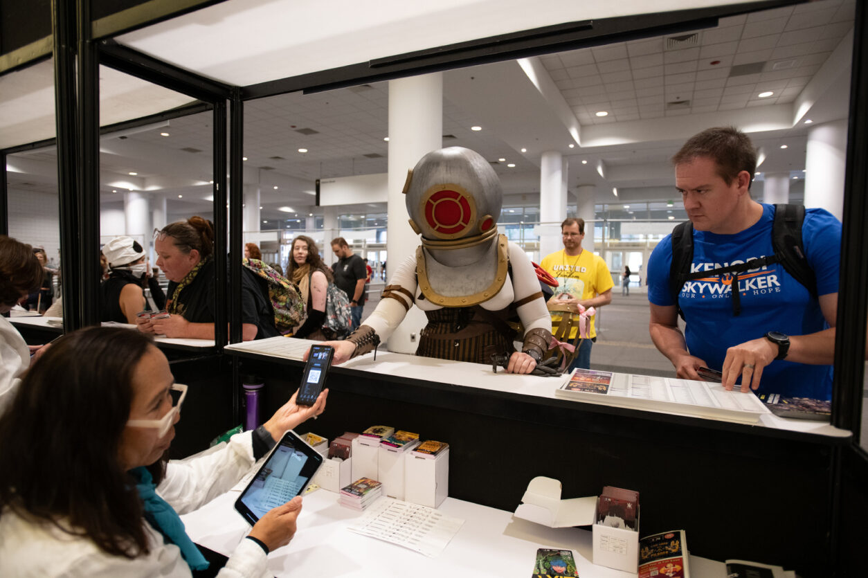 Fans arrive at the show to receive their tickets. One fan in particular is wearing scooba gear, and handing over their QR code to be scanned by staff. Attendees around are smiling at the interaction