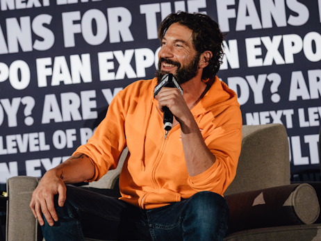 Jon Bernthal sitting on a chair on stage, smiling and holding a microphone.