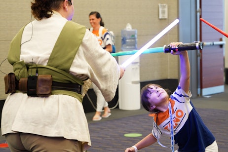 A young fan in Ahsoka merch poses underneath a blue lightsaber