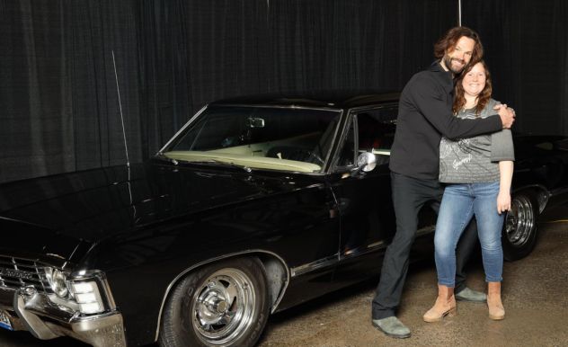 Jared Padalecki poses with a fan in front of the black Chevy Impala - he hugs this fan around the shoulders for the photo