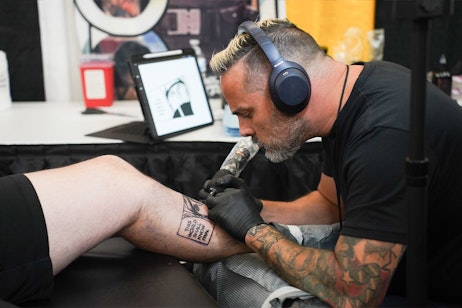 A tattoo artist tattoos art onto a fans leg
