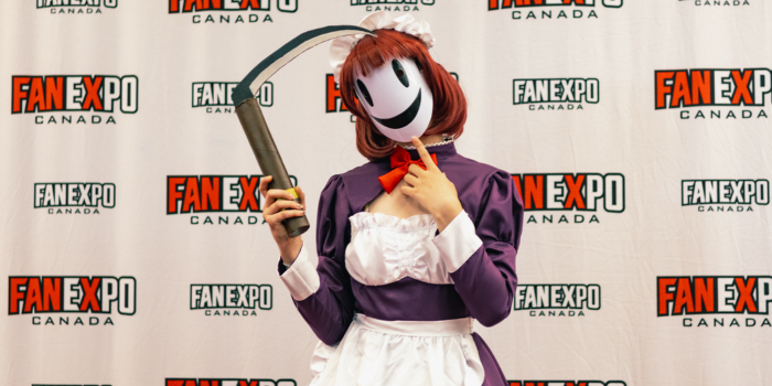 A fan dressed as Mask Maid from High-Rise Invasion poses with a scythe on the Cosplay Red Carpet.