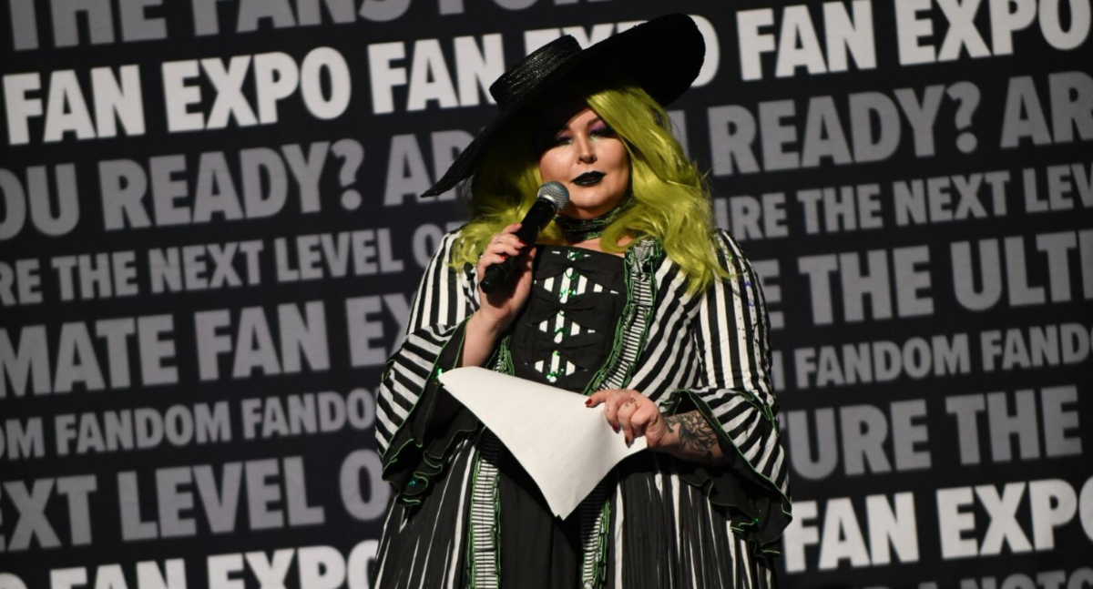 Our Exhibition host LuckyGrim, holding the microphone and addressing the audience. She is dressed as Beetlejuice