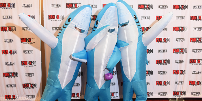 Three fans dress as sharks, in inflatable costumes, pose together with the arms extended in excitement