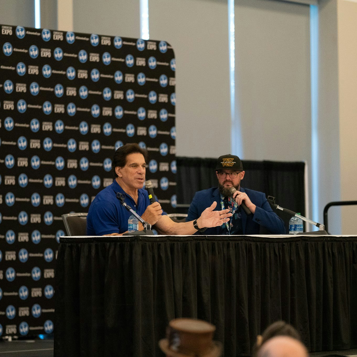 Lou Ferrigno sitting at a table and talking into a microphone