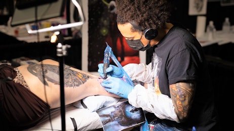 A tattoo artist is designing a tattoo on a fan's leg