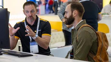 Two men sitting and talking in front of a computer.