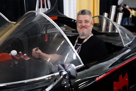 A fan poses happily in a batmobile