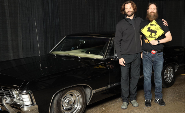 Jared Padalecki poses with male fan in front of the show's Chevy Impala - the fan holds a yellow sign that reads "Moose Crossing"