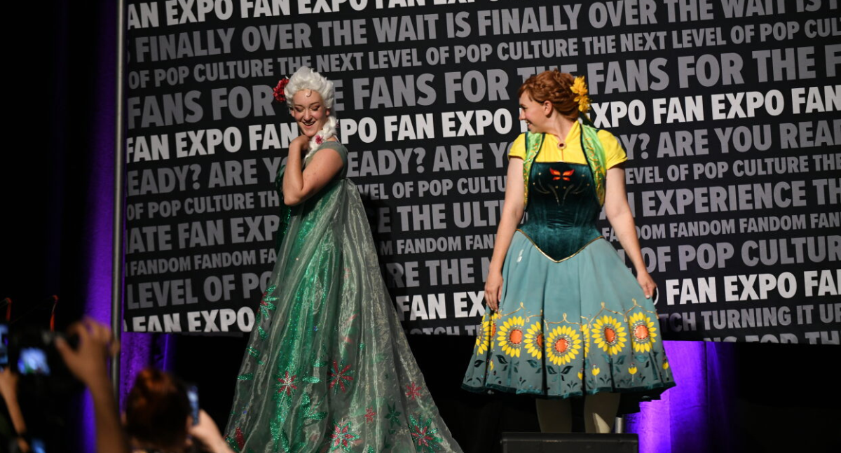 Queen Elsa and Princess Anna dressed in their spring best. Anna's dress features sunflowers and a monarch butterfly, and Elsa's is green and covered in small pink flowers