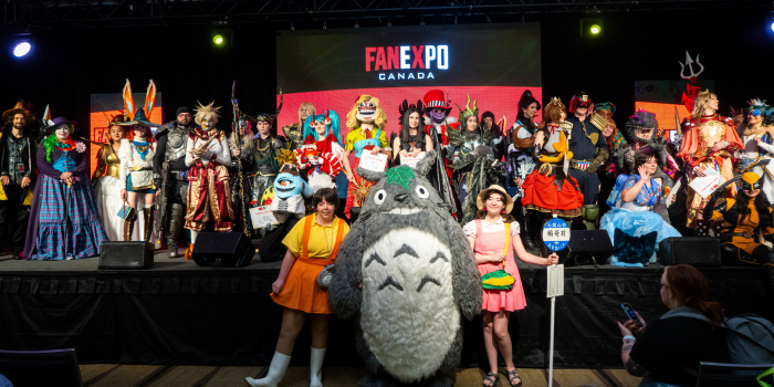 All of the Masters of Cosplay competitors together in a group on stage. Larger cosplayers line up across the front of the stage. Everyone is all smiles.