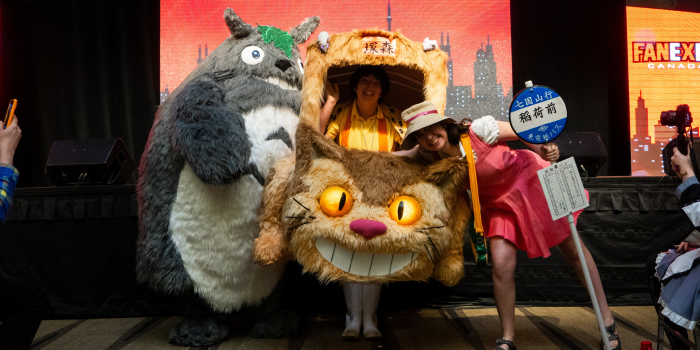 A cosplay trio stands in front of the stage. From left to right: Totoro, Cat Bus, Mei.