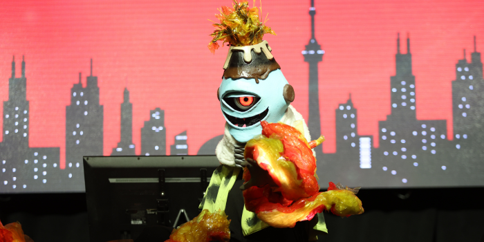 A cosplayer dressed as Jogo from Jujutsu Kaisen , extends their hand to the audience as the fire props light up.