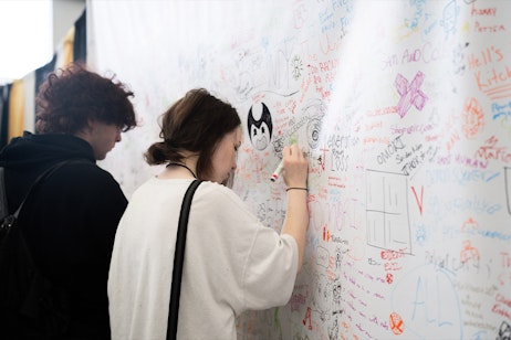 Fans writing their favorite fandom on a white tarp in sharpie