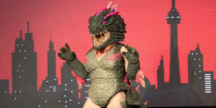 A pink and green glowing Godzilla poses with their claws up for the audience.