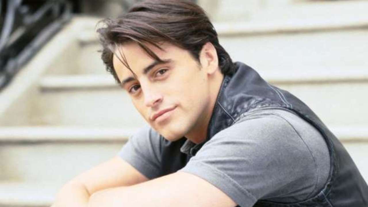 Matt Leblanc smiles at the camera while wearing a grey t-shirt with a black leather vest over top.