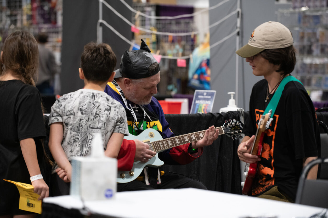 A FAN EXPO Denver VIP teaches kids in Pop Culture Classroom's School of Rock how to play guitar