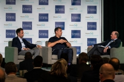 Panel of 3 presenters sitting onstage in chairs at the investors summit