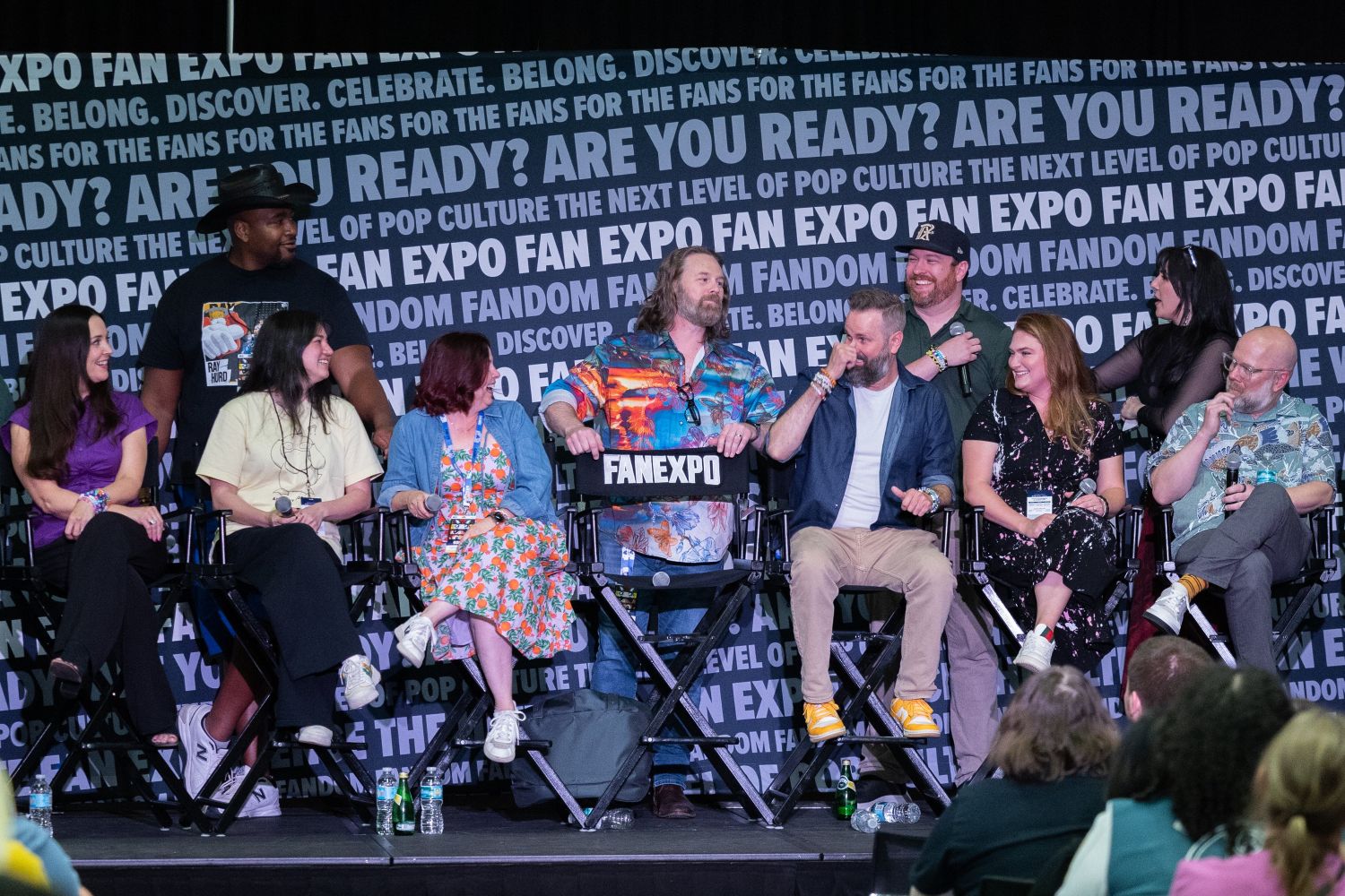 Anime voice actors and creators sit on stage during a lively panel at Dallas FAN FESTIVAL. They smile and laugh together while answering fan questions against a FAN EXPO–branded backdrop.