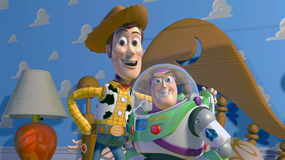 Woody and Buzz stand on Andy's bed, smiling at the screen. Woody's arm is around Buzz.