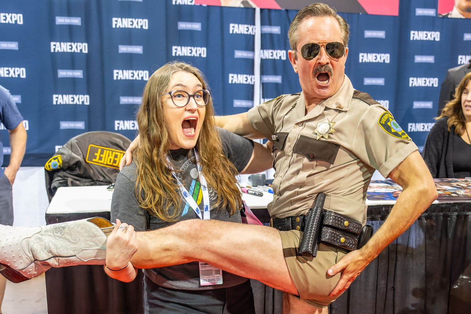 Thomas Lennon, dressed in his Reno 911! sheriff’s uniform and cowboy boots, strikes an exaggerated pose with a fan. Holding up the fan’s leg dramatically, both make hilarious, over-the-top facial expressions, earning big laughs on the red carpet.