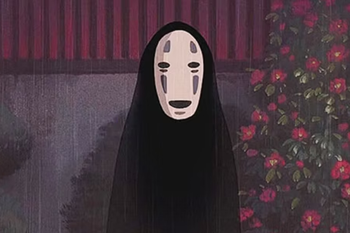 A figure with a white mask and black cloak looks at the camera as it rains