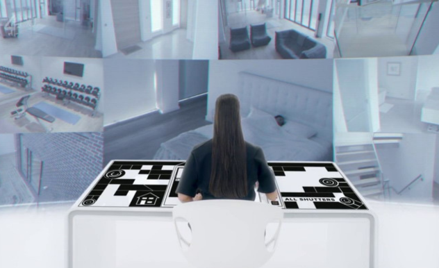 A woman sits at a control board watching a large screen of cameras - each displaying a different room, completely white.
