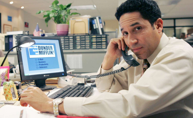 Sitting in front of his computer at his desk, Oscar dials his landline phone to make a call.