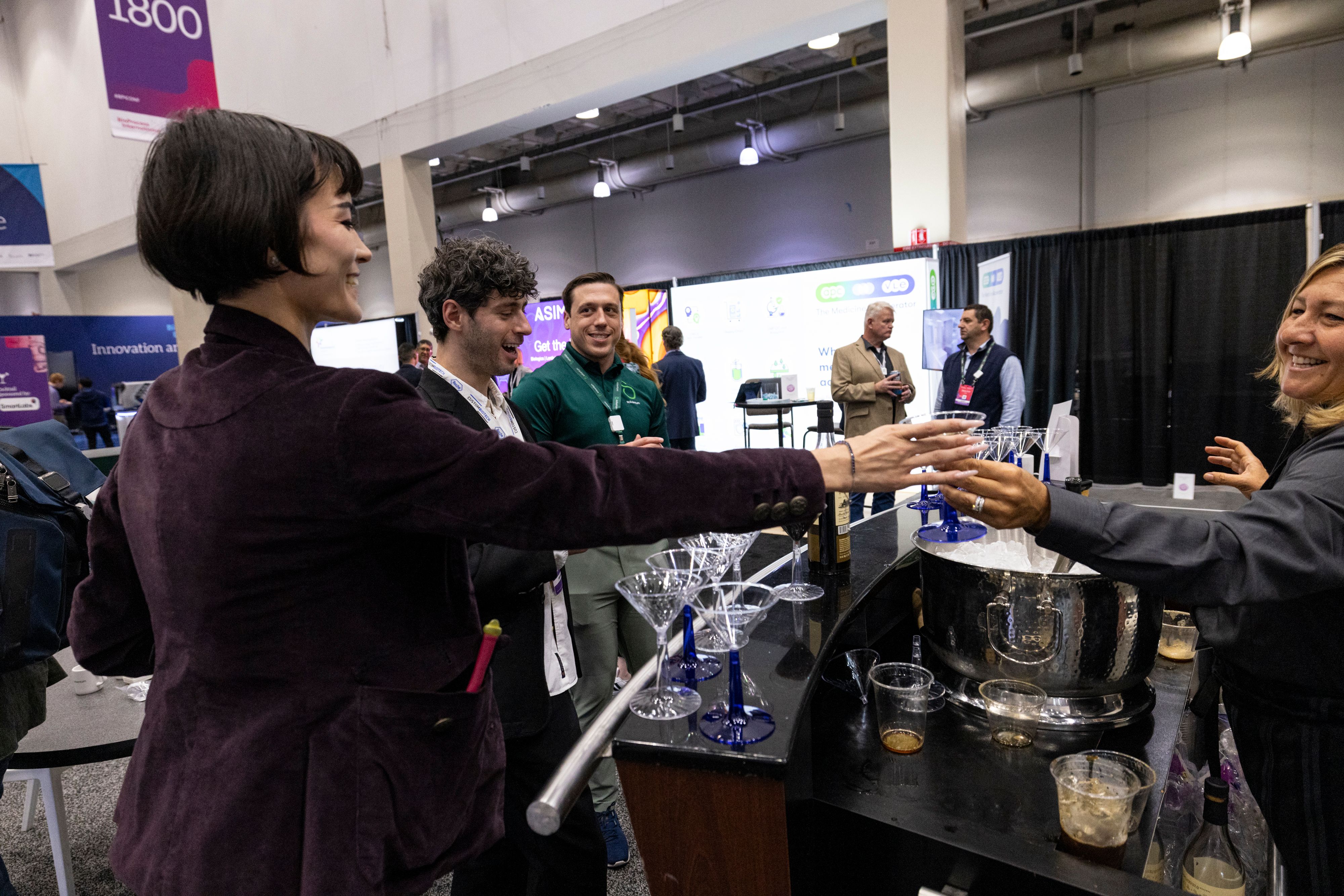 A female attendee at BioTech Week Boston takes a drink from a server in the exhibit hall.