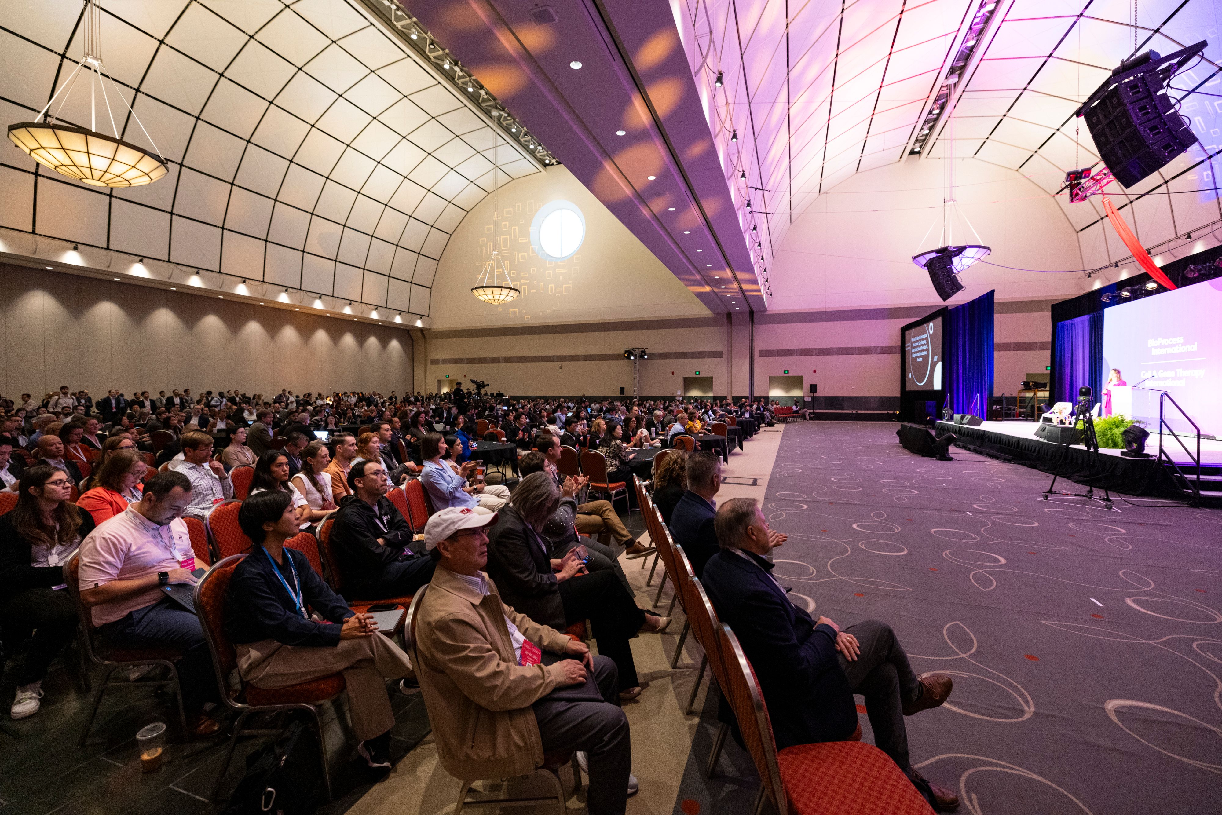 Biopharma attendees sit in a large conference room watching a speaker on stage at BioProcess International (BPI).