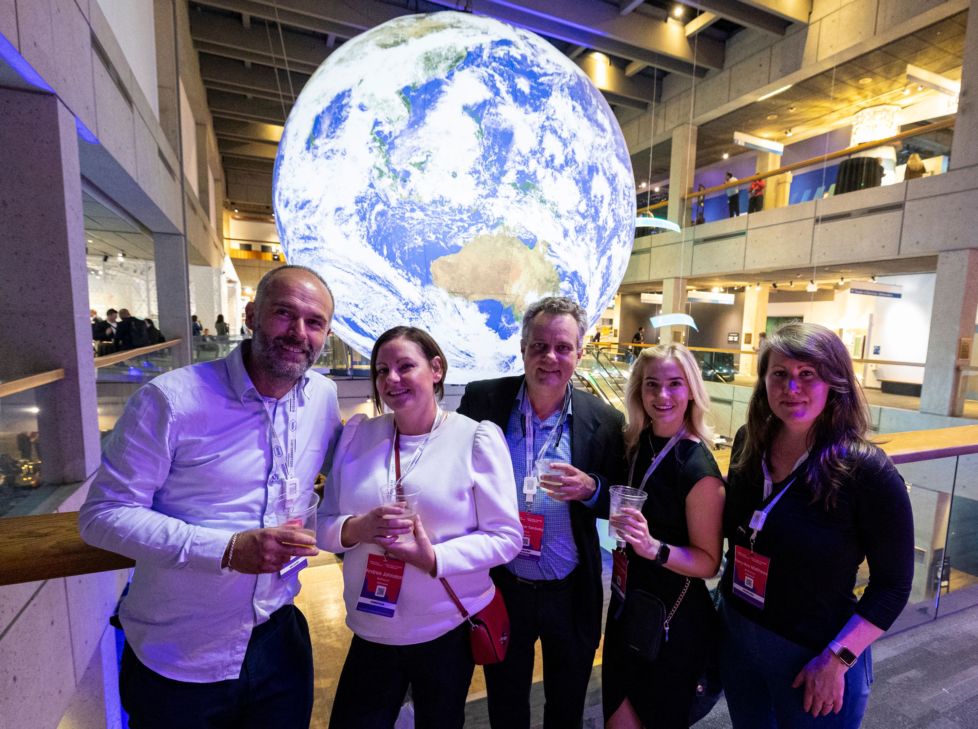A group of five BioTech Week Boston attendees pose for a picture in front of a large, hanging illuminated globe.