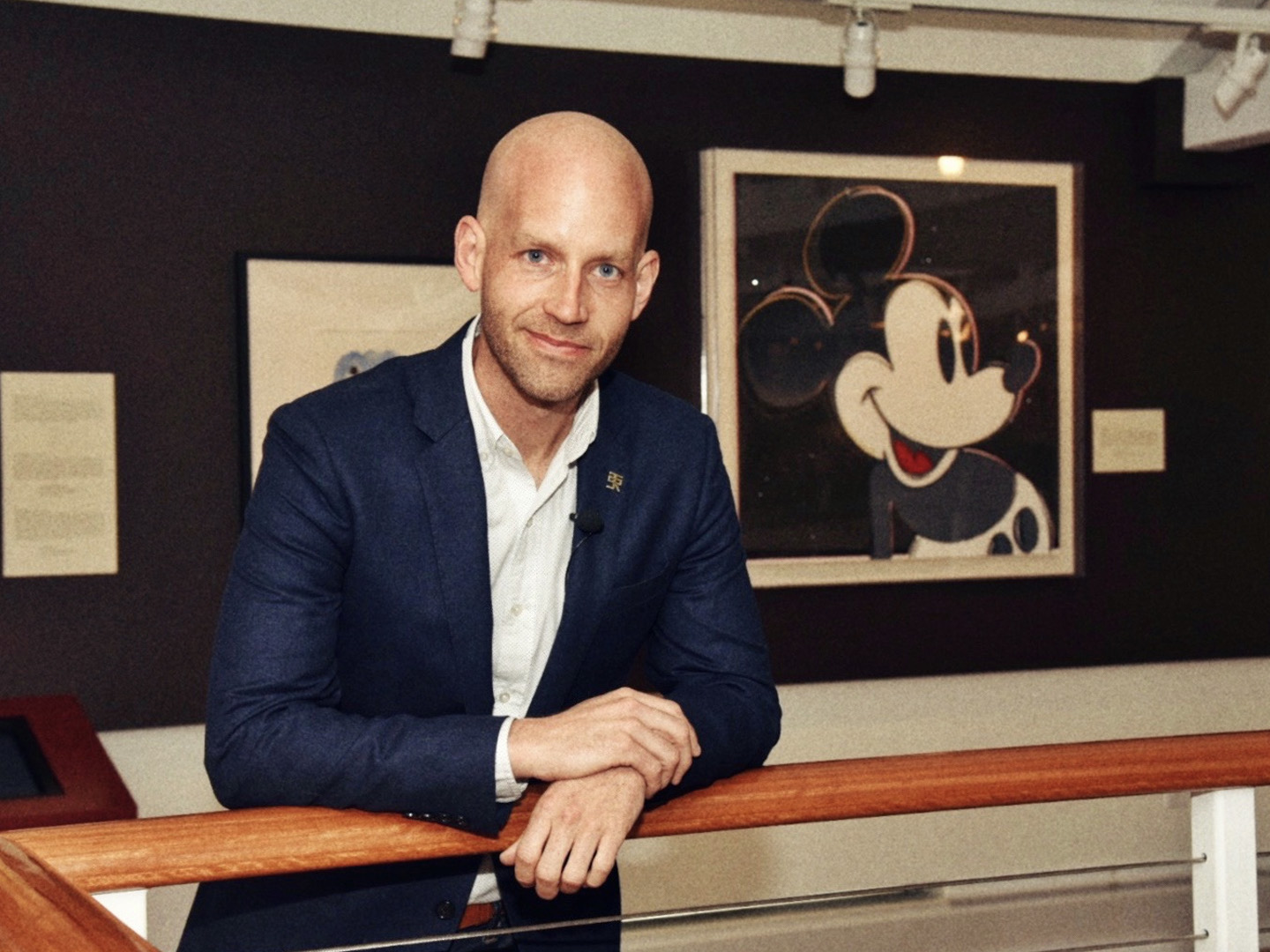 Bret Iwan posing next to a photo of classic Mickey Mouse