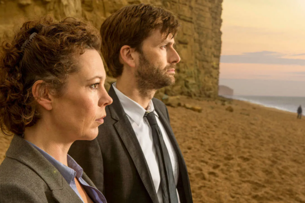 Olivia Coleman and David Tennant standing on a beach and looking out to the water