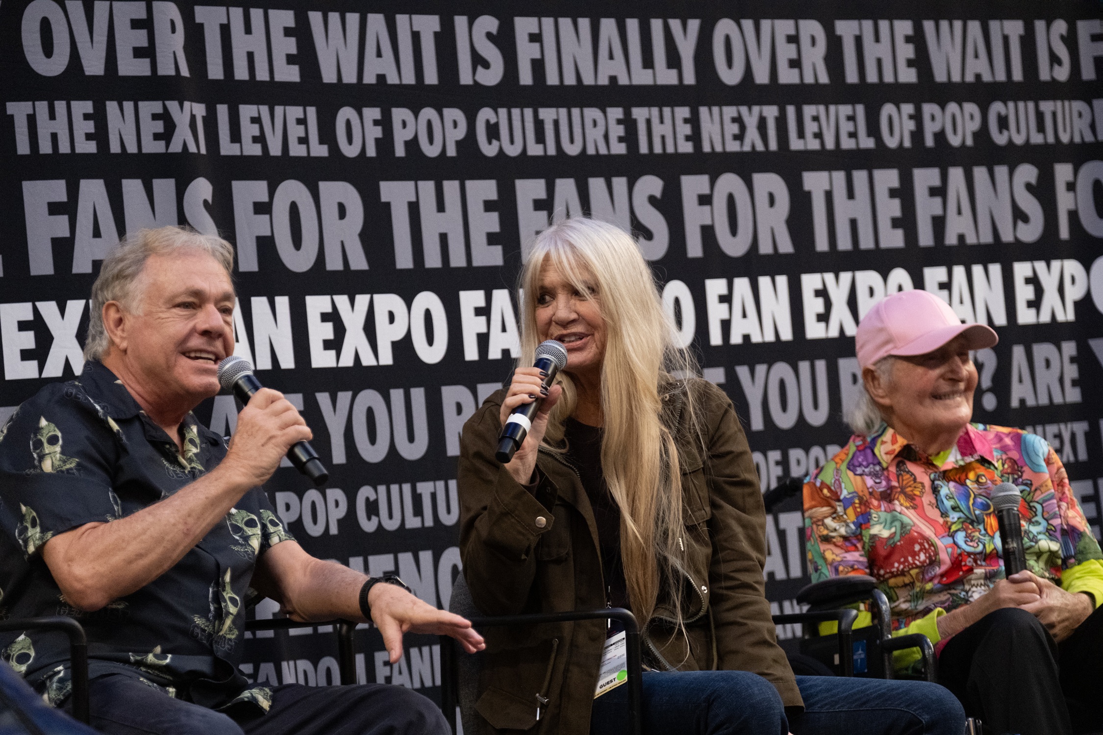 Wesley Eure, Kathy Coleman, and Sid Krofft speak on stage, smiling as they reminisce about their classic series during a lively discussion with fans.