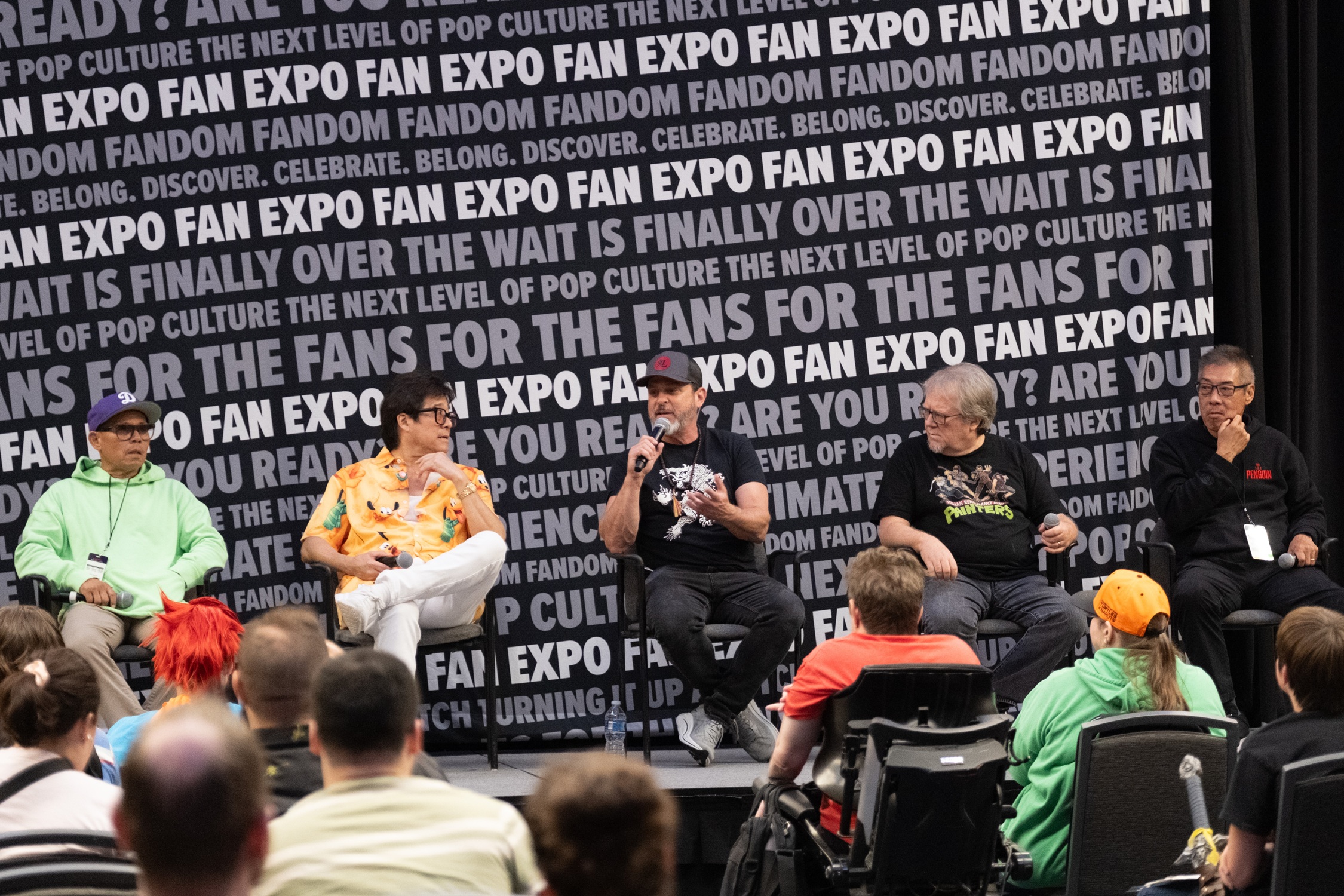 Ernie Reyes Jr., Brian Tochi, Kenn Scott, Robbie Rist, and François Chau take part in a Teenage Mutant Ninja Turtles reunion panel, chatting and laughing together before an engaged audience.
