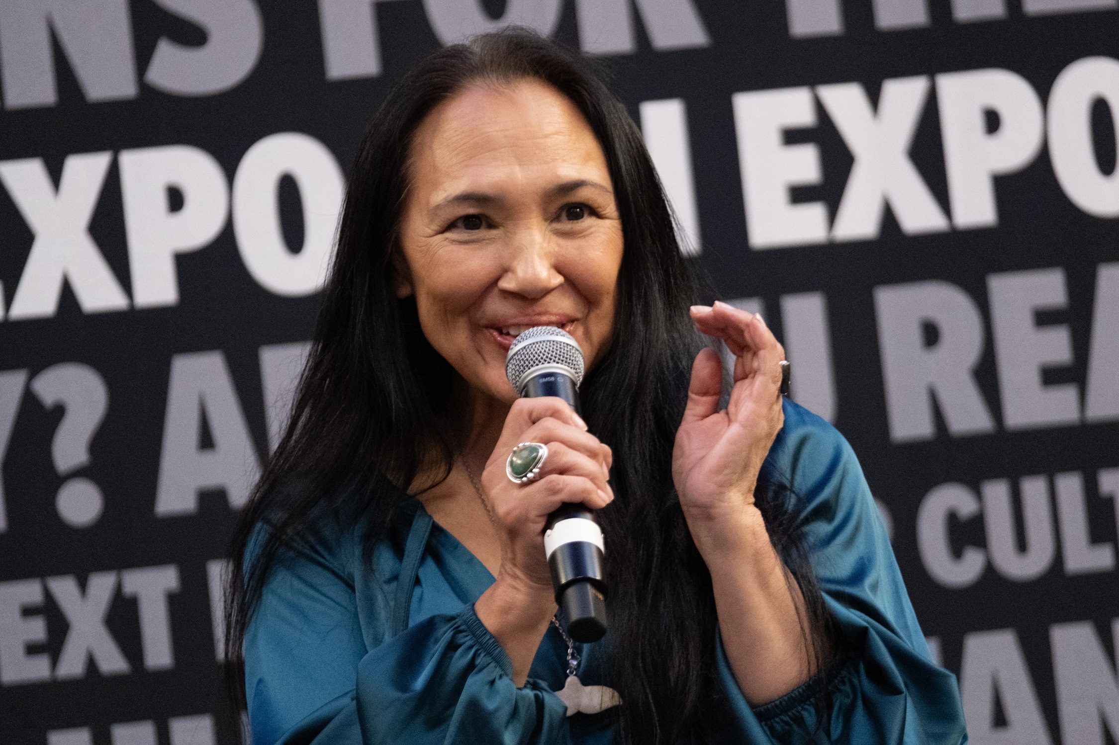Actor Irene Bedard speaks passionately during her panel, holding a microphone and gesturing as she addresses the crowd.