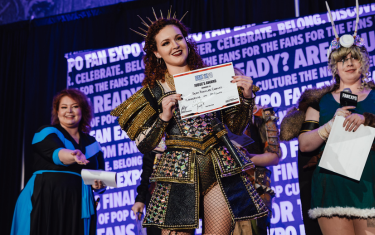 A woman cosplaying as Catherine of Aragon posing with her "Judge's Award" at the Cosplay Craftsmanship Cup.