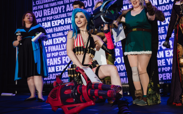 A woman cosplaying as Jinx posing with her "Host's Award" at the Cosplay Craftsmanship Cup.