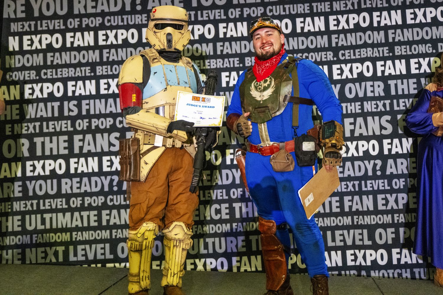 A cosplayer in a detailed Star Wars Shore Trooper costume holds a “Judge’s Award” certificate while standing next to a fellow cosplayer in a Fallout-inspired jumpsuit with a red bandana and armored chest piece.