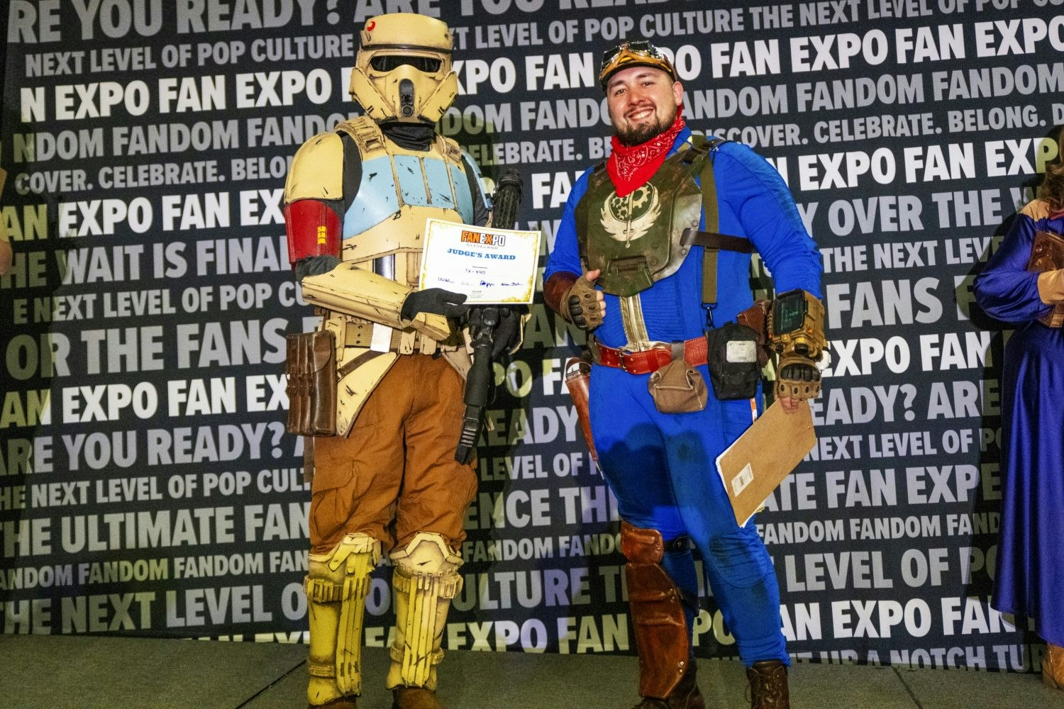 A cosplayer in a detailed Star Wars Shore Trooper costume holds a “Judge’s Award” certificate while standing next to a fellow cosplayer in a Fallout-inspired jumpsuit with a red bandana and armored chest piece.